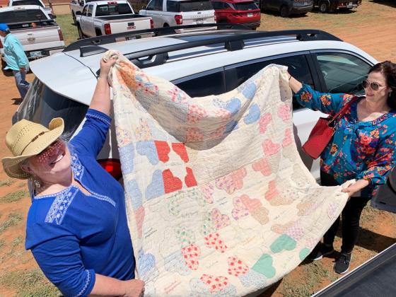 STITCHED WITH LOVE An old friendship quilt bears the names of some Turkey quilters. Sheila Smith and Barbara Brannon (in hat) display the quilt in the midday sun on Bob Wills Day in the Bob Wills Museum parking lot. Smith took the quilt to Turkey in hopes of finding it a home. | PHOTO BY HANABA MUNNWELCH